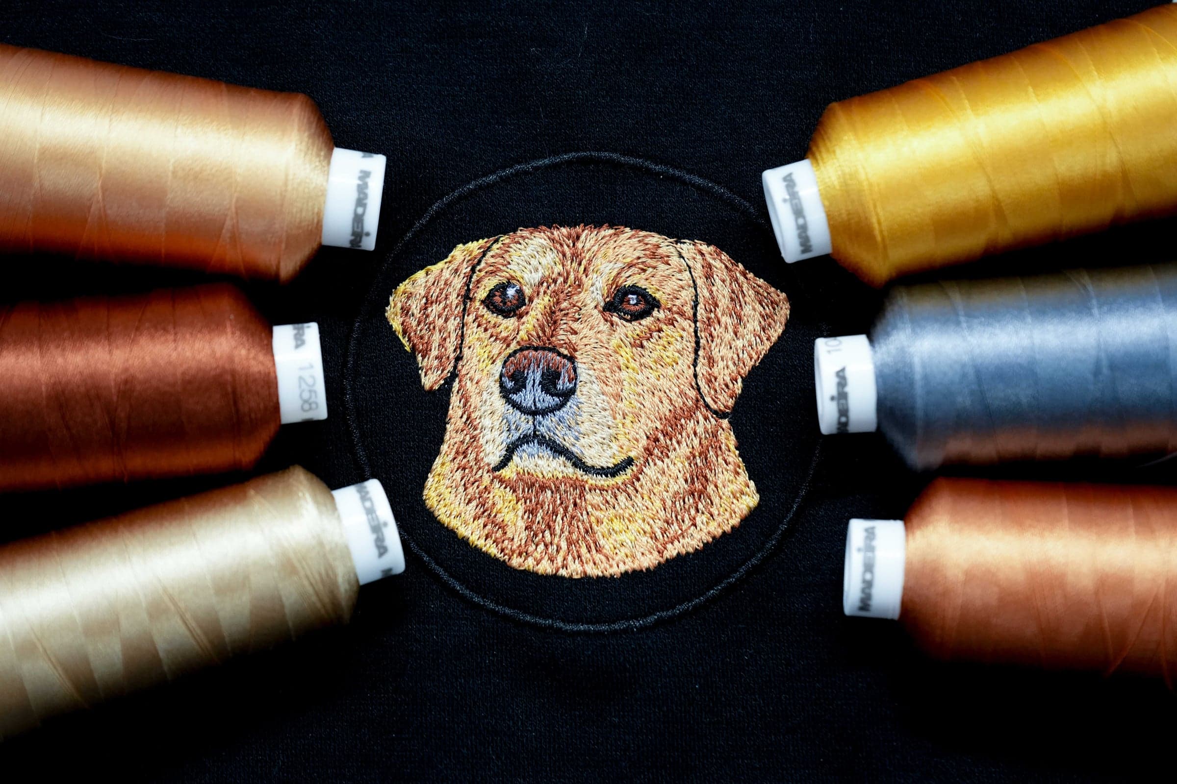 Realistic Labrador embroidery portrait surrounded by Madeira thread spools